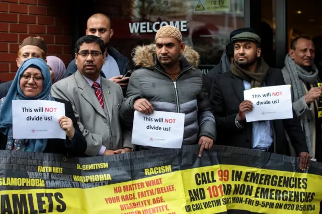 People hold signs saying outside a mosque in East London