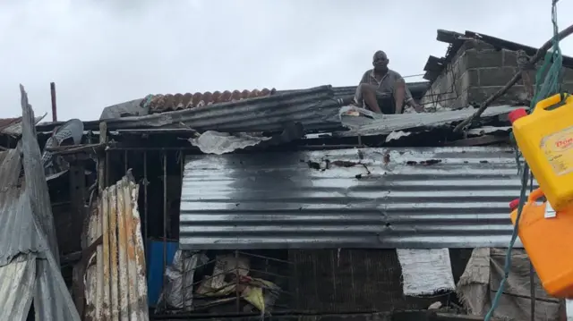 A man sits on on a househould roof made of corrugated iron, Beira, Mozambique