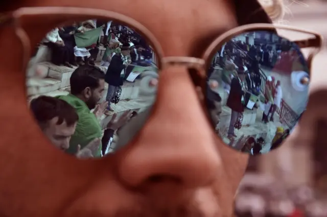 A man wearing sunglasses reflects images of protesters