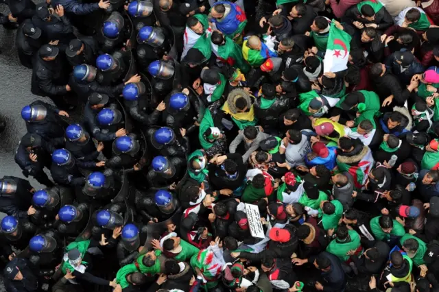 Algerian policemen block the way in front of people protesting against extending President Abdelaziz Bouteflika mandate in Algiers