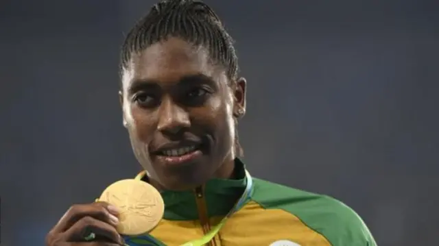 Caster Semenya stands on the podium, holding her Olympic gold medal.