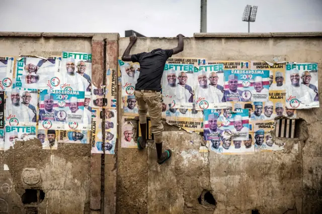 An All Progressives Congress (APC) party supporter climbs up a wall plastered with old election posters during a rally to celebrate the re-election of the incumbent president and the leader of APC