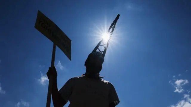 An anti-fracking protester wears a drilling derrick shaped hat during a protest