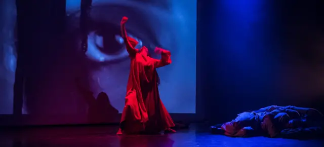 Dancer bathed in red light with backdrop of an eye as part of The Troth