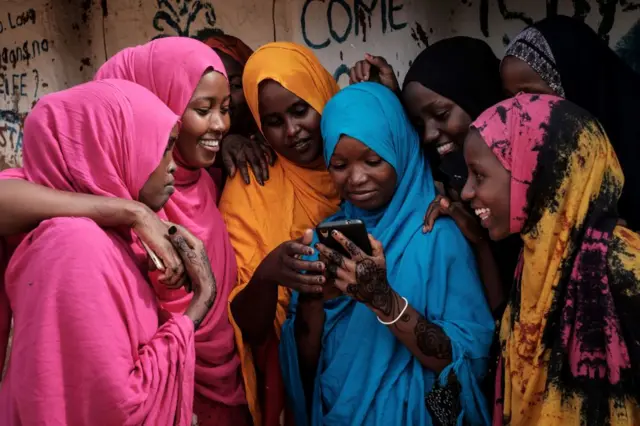 oung Somali refugee women look at a smartphone as they stand together at Dadaab refugee complex, in the north-east of Kenya, on 16 April 2018.