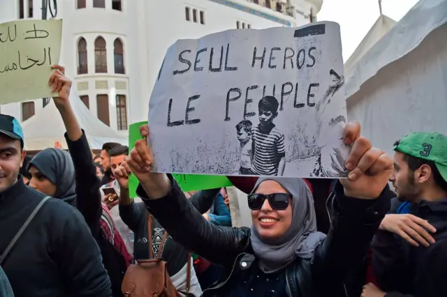 A woman in the crowd holds a sign up.