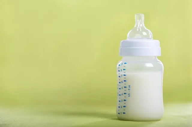 A bottle of formula milk against a green background