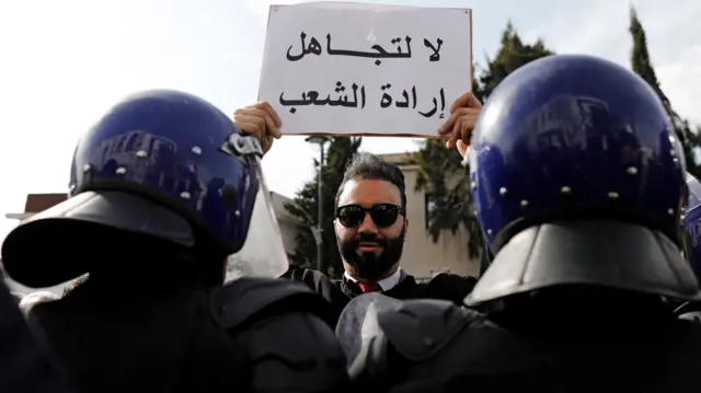 A lawyer holds up a banner near riot police during a protest against President Abdelaziz Bouteflika - 7 March 2019