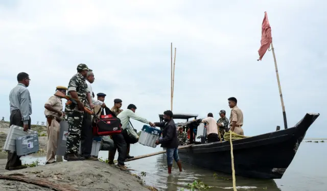 Indian officials and paramilitary police carry voting material along a river in the north-eastern state of Assam.