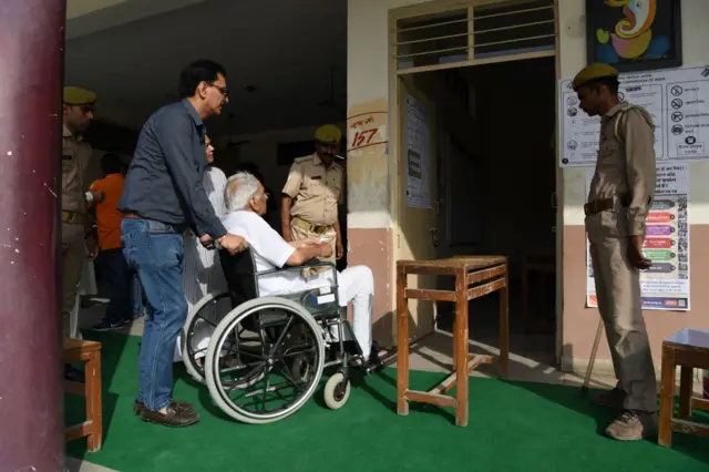 People (L) line up to vote next to security personnel at a polling station during India's general election in Ghaziabad, Uttar Pradesh on April 11, 2019