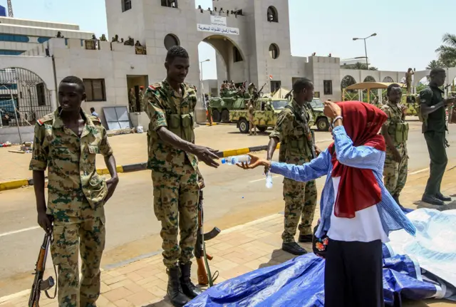 A Sudanese woman hands a soldier a bottle of water during a rally demanding a civilian body to lead the transition to democracy, outside the army headquarters in the Sudanese capital Khartoum