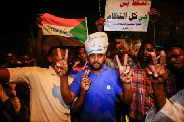 Sudanese protesters flash the victory gesture and raise a sign reading in Arabic "Just fall, that is all, the whole regime".