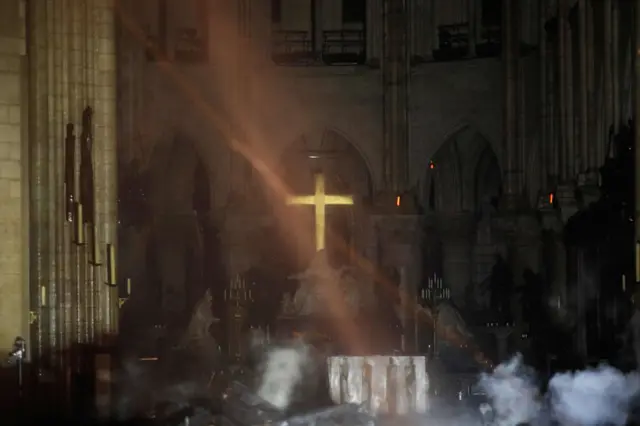 Smoke rises around the alter in front of the cross inside Notre-Dame Cathedral as the fire continues to burn