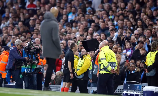 Pep Guardiola looks on as the referee assesses VAR footage on a screen at the side of the pitch