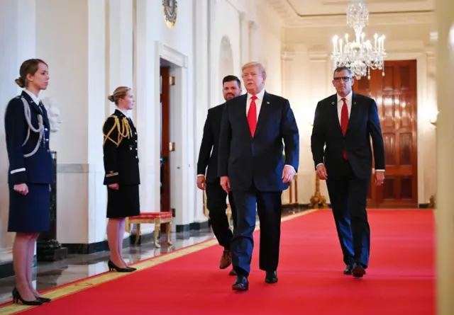 US President Donald Trump (C) flanked by Jose Ramos (L) and Michael Linnington (R), both from The Wounded Warrior Project, walks through the Cross Hall for an event