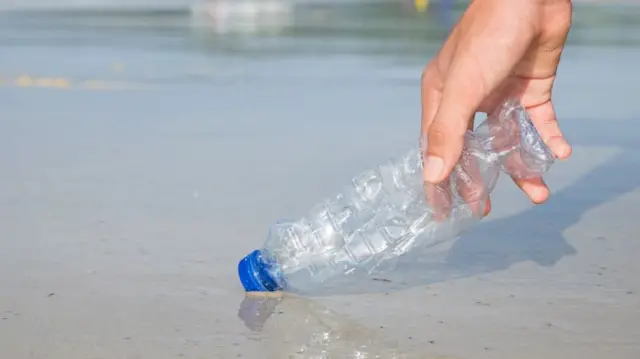 A hand picks up a plastic bottle