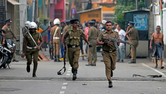 Sri Lankan police clear the area while Special Task Force Bomb Squad officers inspect the site of an exploded van near a church that was attacked in Colombo, Sri Lanka