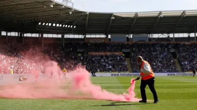 A steward removes a flare thrown onto the pitch