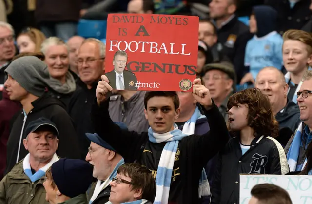 A Manchester City fan holds up a banner describing David Moyes as a football genius