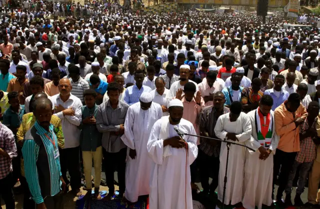 Imams and protesters stand in prayer outside