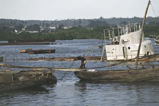 A pirogue in front of the wreck of a ship, port of Stone Town, Zanzibar, Unguja Island, Tanzania.