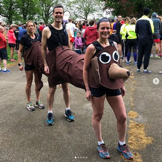 Two women and a man in their running gear standing inside one sausage dog costume