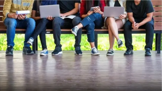 People sitting on a bench, some with laptops or tablets