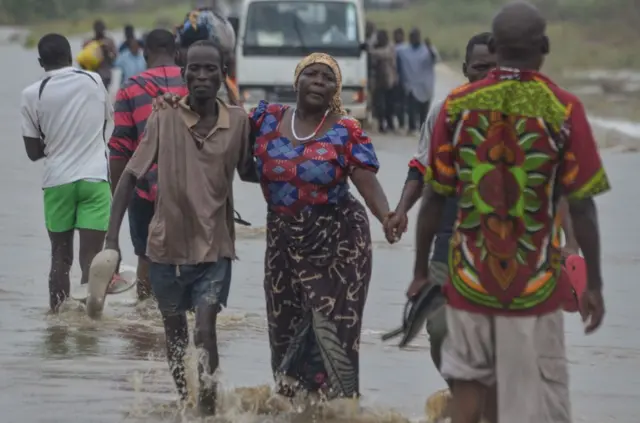 Residents help a woman crossing a flooded street in Mazive, southern Mozambique,