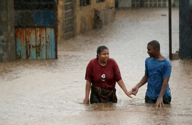 A man helps a woman through a flooded neighbourhood in the aftermath of Cyclone Kenneth, in Pemba, Mozambique, April 28, 2019