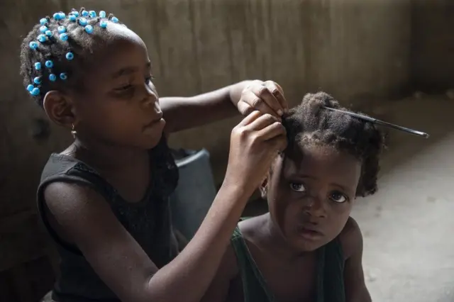 On Monday, this Mozambican girl sits patiently as another child braids her hair at the temporary aid shelter they are now living in because of the devastation wrought by the storm.