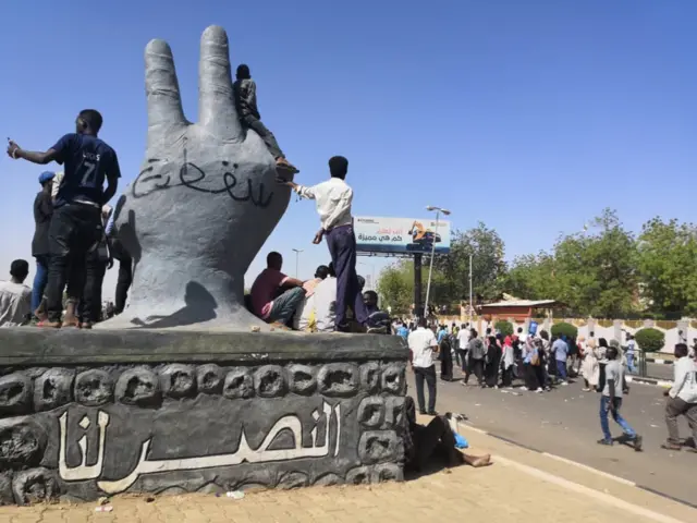 Sudanese protesters stand on a monument as others rally in the area of the military headquarters in the capital Khartoum on April 8, 2019