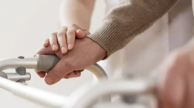 Hand on elderly person's hand on a walking frame