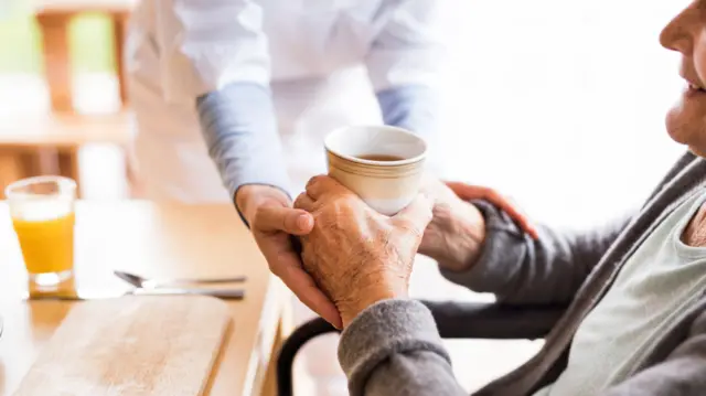 Unrecognizable health visitor or nurse giving tea to an elderly woman