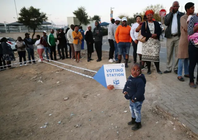 A child looks on as voters queue to cast their ballots outside a polling station in Alexandra township in Johannesburg, South Africa, May 8, 2019