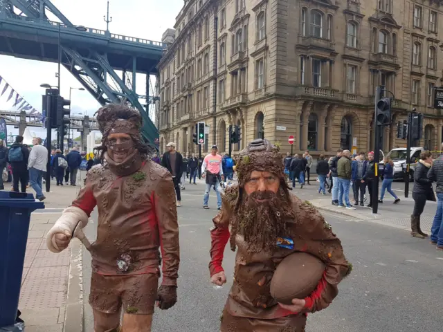 Two fans dressed as if they are covered in mud