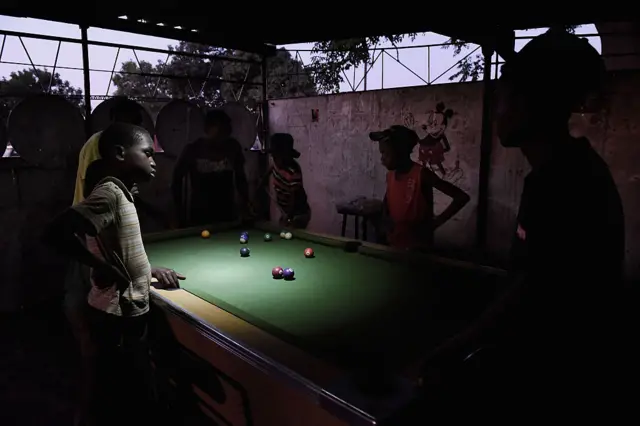 Young boys play pool by torchlight in the gathering darkness in the town of Chitungwiza where electricity is only provided for a few hours, usually late at night, in Chitungwiza, Zimbabwe, on October 8th 2015.