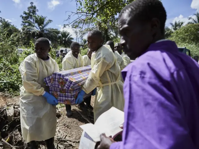 Health workers help bury the coffin of an Ebola victim