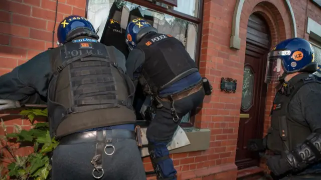 Police officers climb through a broken window