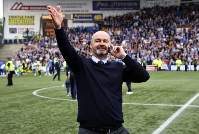 Steve Clarke shares a wave with the crowd as he has a word on the phone with someone