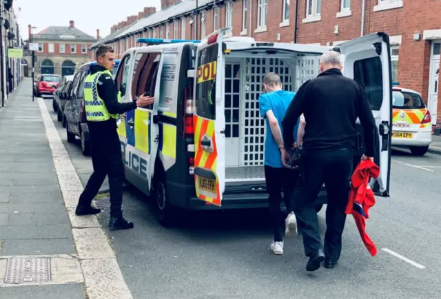 An arrested man is put in the back of a police van