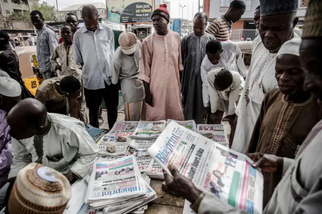 Men stand around a newsstand with national newspapers bearing headlines announcing the victory of the incumbent President Muhammadu Buhari following Nigeria's presidential election result on February 27, 2019, in Kano. -