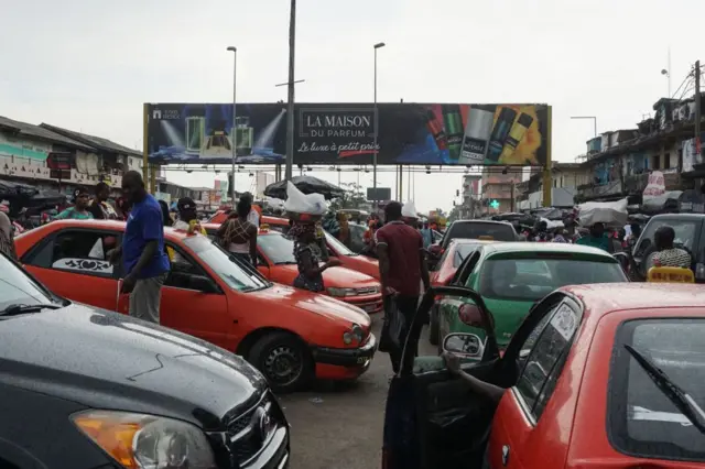 People walk near cars at the Adjame market in Abidjan, on May 3, 2019.