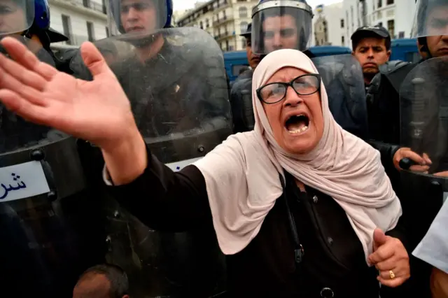 An Algerian woman shouts slogans as security forces stand guard during an anti-government demonstration in the capital Algiers