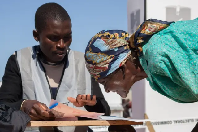 A woman with vision problem squints close to a ballot paper to see images and symbols of candidates to enable her vote at the Goliati Primary School in Goliati village