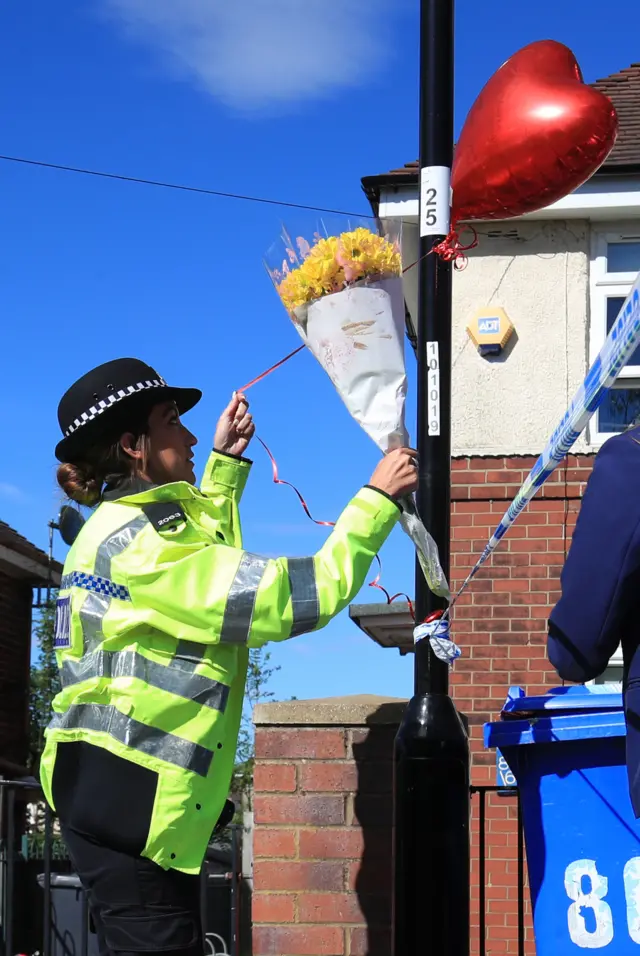 Policewoman hanging a balloon and flowers to a pole