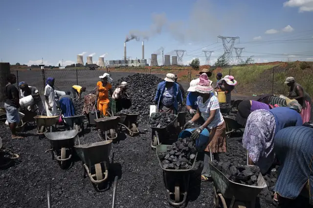 Women from the coal dust covered and power line pollution exposed Masakhane settlement fill their wheel barrows for a load of free coal provided by a nearby mine on February 5, 2015 in Emalahleni.