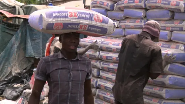 A man carries a bag of cement on his head on a construction site