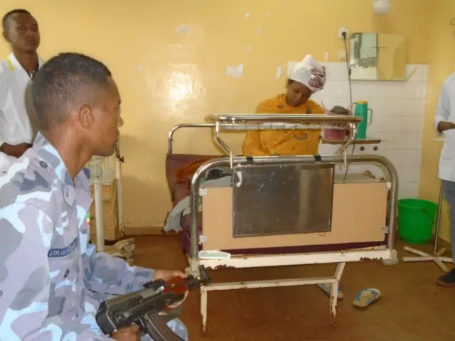 Man holding a gun looking at woman in a hospital bed