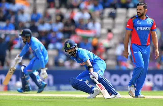 Gulbadin Naib (R) looks on as India"s captain Virat Kohli (C) runs between the wickets with India"s K.L. Rahul