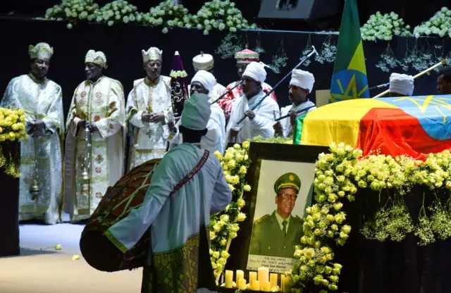 Religious leader gather on stage by coffins covered with the Ethiopian flag.